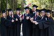 © Михаил Решетников - A group of graduates in robes give a thumbs up outdoors. Elderly student.