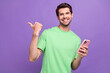 © deagreez - Photo of clever funny man with stubble green t-shirt hold smartphone directing at sale empty space isolated on purple color background