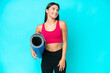 Young sport caucasian woman going to yoga classes while holding a mat isolated on blue background thinking an idea while looking up