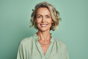 Portrait of beautiful middle aged woman smiling at camera while standing against green background