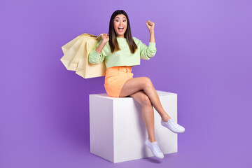 Sticker - Full length photo of ecstatic overjoyed girl wear stylish pullover sit on platform buy new clothes isolated on violet color background