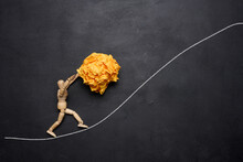 A Wooden Figurine Of A Person Rolling A Crumpled Paper Ball Upwards, Concept Of Perseverance And Hard Work, Achieving Goals.