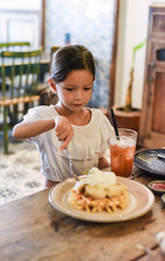 Wall Mural - Little asian girl eating sweet belgian waffles with banana and cream in a cafe