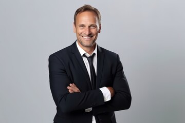 Wall Mural - Portrait of a smiling mature businessman with arms crossed standing against grey background