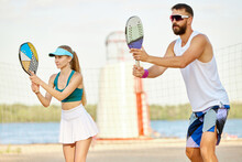 Team. Young Man And Woman Playing Paddle Tennis On Beach On Warm Summer Day Near River. Outdoor Activity. Concept Of Sport, Leisure Time, Active Lifestyle, Hobby, Game, Summertime, Ad