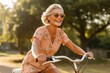 © igolaizola - happy senior woman in sunglasses riding bicycle in park on sunny summer day