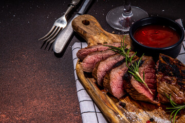 Wall Mural - Grilled meat steak on dark table, Pork, veal, lamb, beef steak medium, medium well on cutting board, with spices, ketchup bbq sauce, wine glass. Dinner in steak restaurant menu, top view copy space