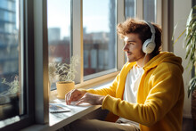 Young Handsome Man In Yellow Clothes Working From Home Near The Window. High Quality Photo