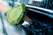 Close-up of a car wash worker using a green washcloth to wash a black luxury car with car wash shampoo