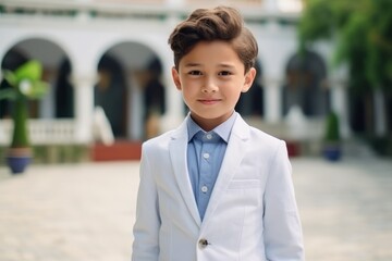 Wall Mural - Portrait of a cute little boy in a white jacket and blue shirt, standing in the courtyard of the mosque