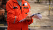 © Nattawit - Action of a supervisor is writing on paper which in clipped on clipboard for taking report during perform safety audit in the construction operation. Industrial safety working scene. Selective focus.