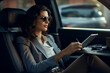 © pangamedia - An adult latin business-woman is working concentrated with computer without logo in the backseat of a expensive modern car while drinking coffee