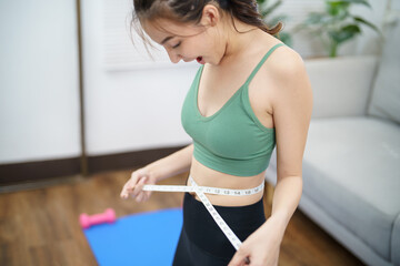 Wall Mural - Asian healthy woman dieting Weight loss. Slim woman measuring waist with measure tape after diet at home weight control.