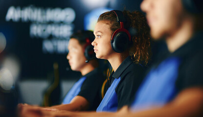 Side view of a focused mixed race girl, female cybersport gamer wearing headphones playing online video games, participating in eSport tournament