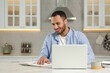 © New Africa - Young man working on laptop at desk in kitchen. Home office
