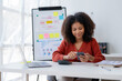 © amnaj - Black businesswoman with curly hair is using smartphone in office.