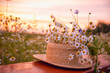 Leinwandbild Motiv A straw hat and a bouquet of wild flowers on a wooden bench in a field at sunset on a summer evening.