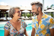 © July P - An older attractive woman flirts with a young man by the pool in a tropical hotel.