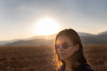 Wall Mural - portrait of a beautiful young girl in glasses on a walk in the mountains. travel in the mountains at sunset.