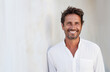 © OPPERMAN - Tanned 40 year old man in white shirt leaning on a white wall.