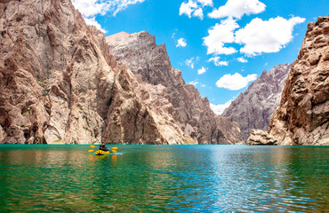 Wall Mural - Kayaking on a mountain lake. Two men are sailing on a yellow canoe along the lake along the rocks. The theme of water sports and summer holidays. 