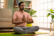 Indian young man doing namaste posture or yoga with closed eyes while sitting at home - concept of healthy lifestyle, fitness and self caring