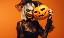 Woman With Halloween Makeup Holding Carved Pumpkin On A Orange Background