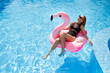 © artiemedvedev - Hot slim woman relaxing on inflatable pink flamingo float mattress in bikini at swimming pool. Attractive fit girl in swimwear lies in the sun on floaty. Pretty female chilling on tropical vacation.