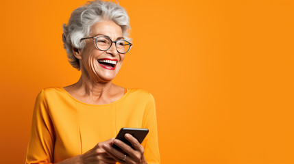 Canvas Print - An elderly woman smiling and laughing with her phone against an orange background.