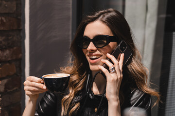 Wall Mural - Blonde woman smiling positive conversation talking to her friend using phone hand hold hot drink coffee relax casual positive emotion weekend relax routine at cafe restaurant. Girl have discussion.