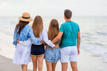 Wall Mural - Family of four have fun together on beach vacation at sunset