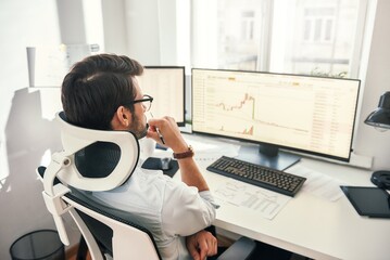 Fototapete - No time to relax. Back view of professional trader working with graph and financial reports on computer screens while sitting in his modern office.