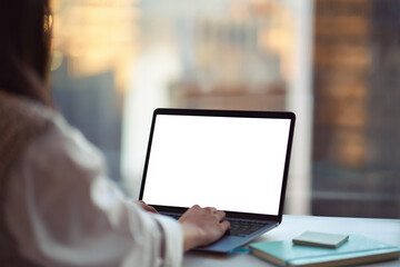 Business woman using laptop in office sitting at desk. Female hands typing on computer white blank mock up empty screen display for business websites or webinars ads. Over shoulder view. Close up