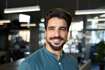 Wall Mural - Smiling young business man looking away in office, headshot close up portrait. Happy Latin businessman, male entrepreneur, professional manager or company employee worker standing at work.