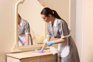 Canvas Print - Young chambermaid cleaning dressing table in hotel room