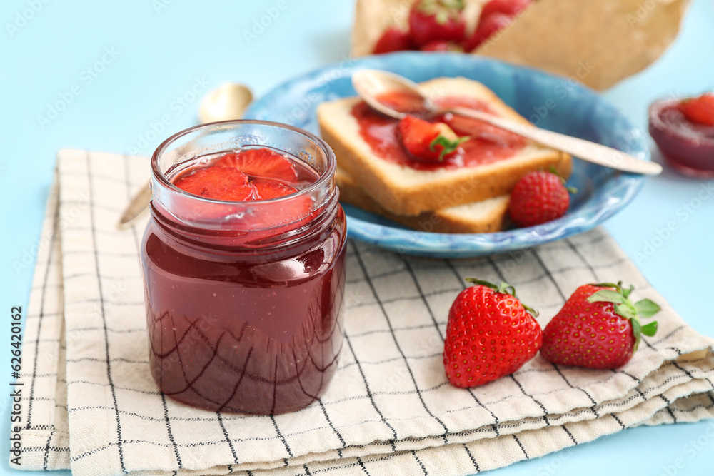 Jar of sweet strawberry jam on blue background