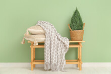 Wooden Bench With Blanket, Cushions And Plant In Wicker Basket Near Green Wall