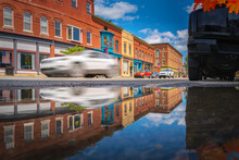 Houlton Downtown And Historic Buildings With Water Reflections Of Passing Cars Over The Rain Puddle After Storm In July