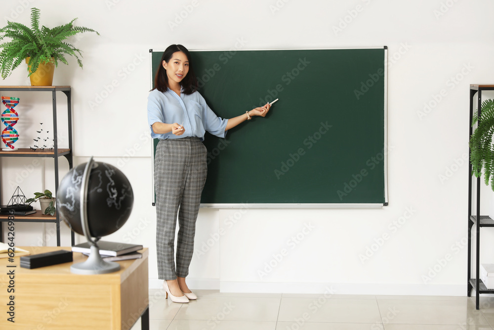 Female Asian teacher near chalkboard in classroom
