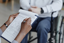 Closeup Of Unrecognizable Nurse Holding Clipboard With Patients Chart While Talking To Man In Wheelchair, Copy Space