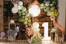 Arch Decorated Green, Brown, Golden Balloons, Neon Numbers One, Paper Leaves. Birthday Cake For 1 Year Old Girl Or Boy On Background Photo Wall, Zone. Reception At Birthday Party. Decor In Style Zoo.