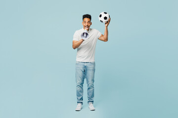 Full body promoter young man fan wearing t-shirt cheer up support football sport team hold in hand soccer ball scream in megaphone watch tv live stream isolated on plain pastel blue color background.