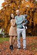 © Anna - Young parents with a baby in their arms against the background of a yellow tree in the park in autumn