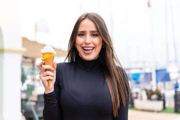 Wall Mural - Young pretty woman with a cornet ice cream at outdoors with surprise and shocked facial expression