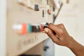 Wall Mural - Closeup of black young man using control panel at factory focus on hand turning switch, copy space