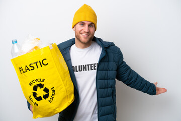 Wall Mural - Young caucasian holding a bag full of plastic bottles to recycle isolated on white background extending hands to the side for inviting to come