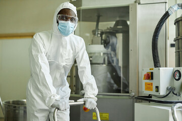 Wall Mural - Portrait of black man wearing mask and protective suit working with chemicals at pharmaceutical factory, copy space