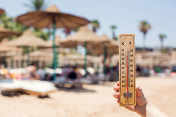 thermometer in hand on a beach background showing high temperature. hot weather and climate concept