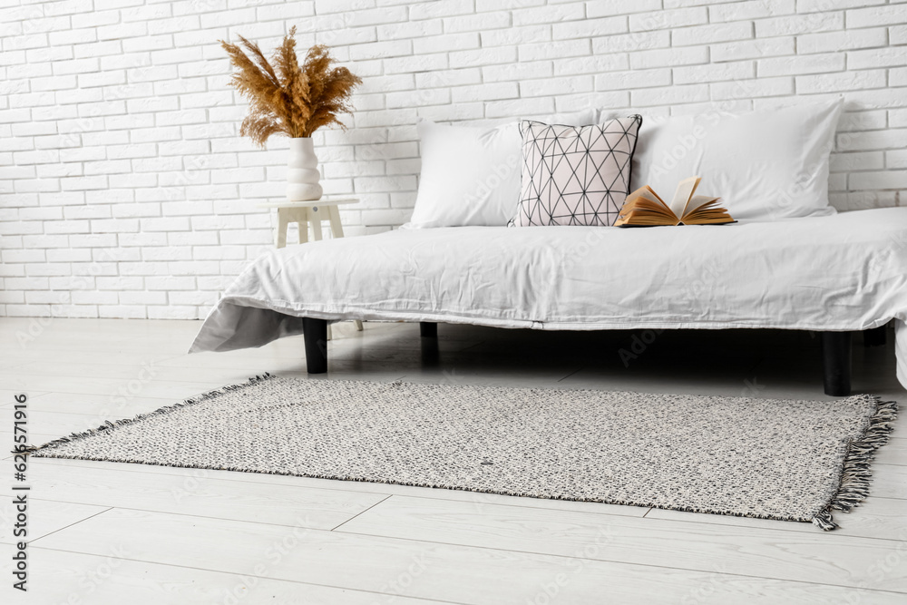 Interior of light bedroom with cozy bed and stylish carpet