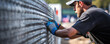 Worker fastening or repair metal mesh fence with hands.